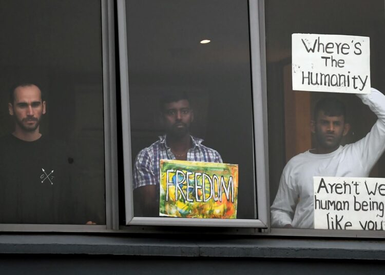 Three asylum seekers gesture to protesters holding a pro-refugee rights rally from their hotel room where they have been detained in Melbourne on June 13, 2020, after they were evacuated to Australia for medical reasons from offshore detention centres on Nauru and Manus Island. (Photo by William WEST / AFP)