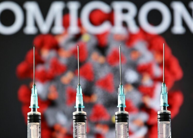 An illustration picture taken in London on December 2, 2021 shows four syringes and a screen displaying the word 'Omicron', the name of the new covid 19 variant, and an illustration of the virus. (Photo by Justin TALLIS / AFP)