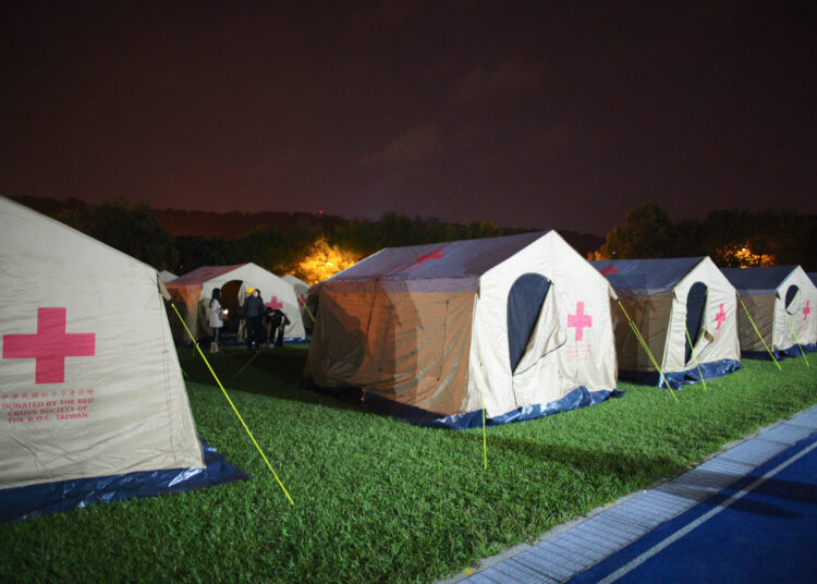 Earthquake affected people stand outside a tent at a temporary reception center set at a local school in Hualien on April 3, 2024, after a major earthquake hit Taiwan's east. - At least nine people were killed and more than 1,000 injured on April 3 by a powerful earthquake in Taiwan that damaged dozens of buildings and prompted tsunami warnings that extended to Japan and the Philippines before being lifted. (Photo by Sam Yeh / AFP)