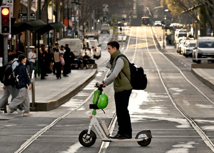A man not wearing a helmet rides an e-scooter from a hire company in Melbourne's central business district (CBD) on August 14, 2024. - Melbourne has become the latest city to announce a ban on rental e-scooters, abruptly moving to end a trial contract with two firms after a community revolt. (Photo by William WEST / AFP)