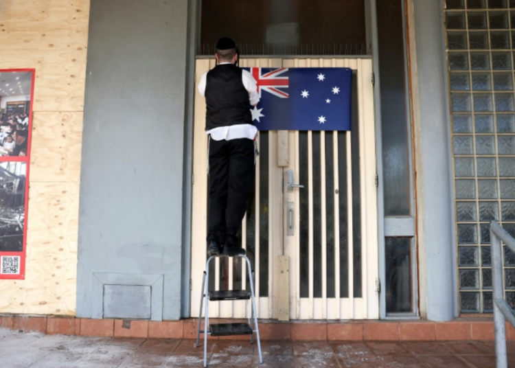 A member of the Jewish community attaches an Australian national flag to the front of the damaged Adass Israel Synagogue in the Melbourne suburb of Ripponlea on December 9, 2024 (Martin KEEP)