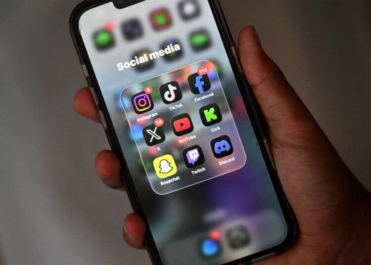 A 13-year-old boy poses at his home as he looks at social media on his mobile phone in Sydney on December 8, 2025. Australia will ban young teenagers from social media on December 10, 2025, launching a world-first crackdown designed to unglue children from addictive scrolling on the likes of Facebook, Instagram and TikTok. (Photo by Saeed KHAN / AFP)