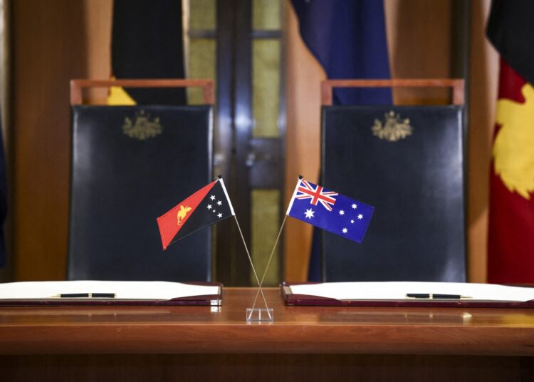 The national flags of Australia and Papua New Guinea are displayed on a desk before Australia's Prime Minister Anthony Albanese and Papua New Guinea's Prime Minister James Marape sign the Pukpuk treaty at Parliament House in Canberra on October 6, 2025. Australia and Papua New Guinea signed a long-awaited mutual defence treaty, as Canberra seeks to deepen ties with Pacific nations and counter Beijing's rising influence. (Photo by DAVID GRAY / AFP)